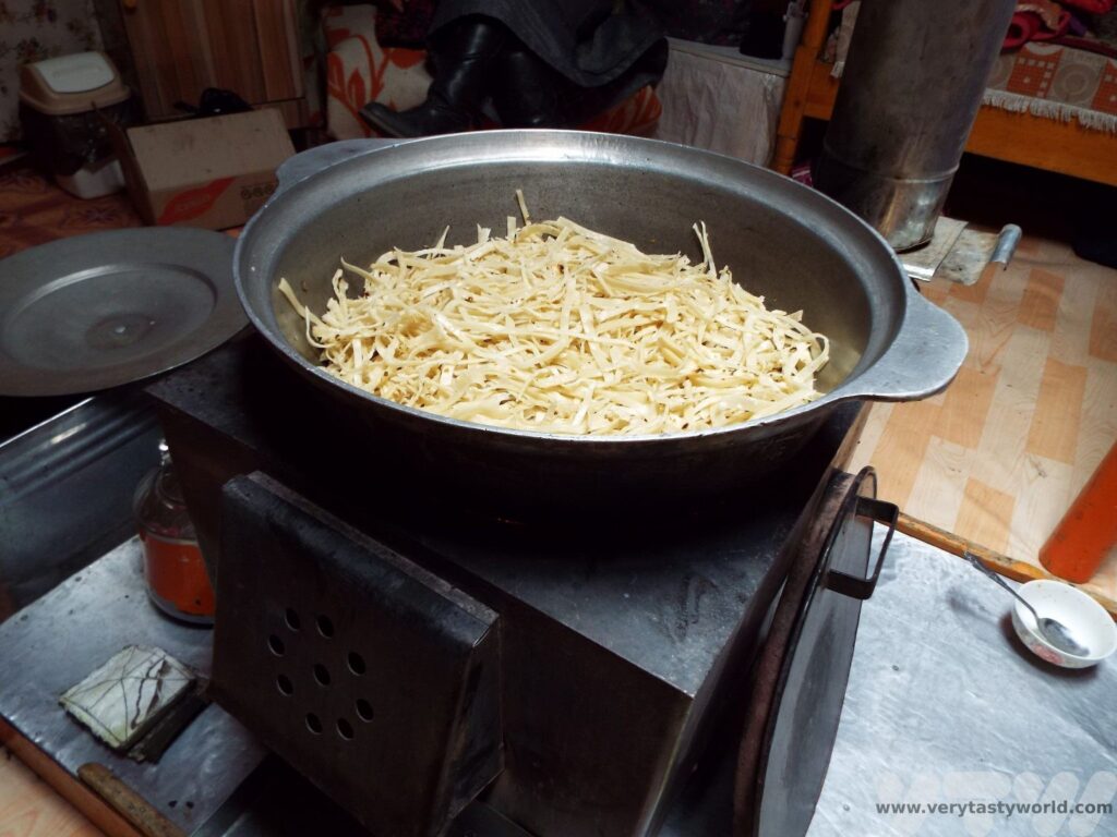 Making Tsuivan in a ger in Mongolia - lay the noodles on the meat and cook