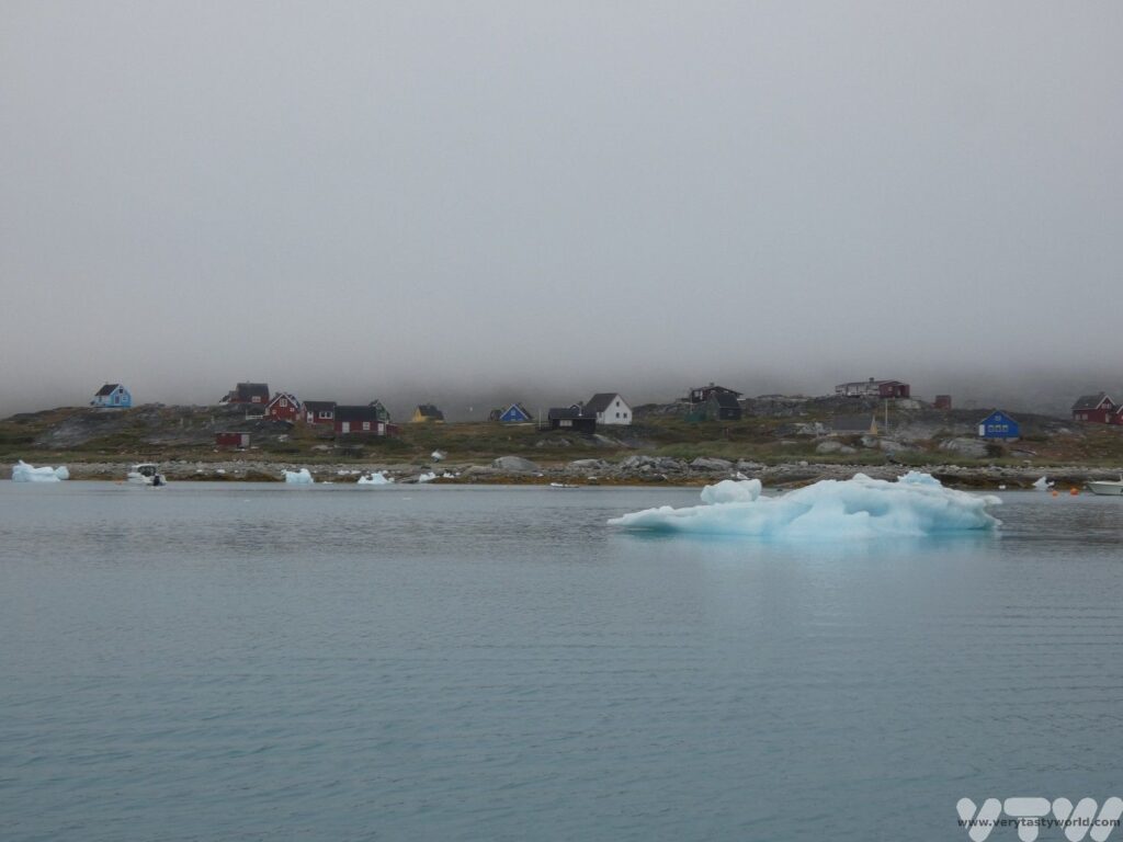 The colourful houses of Qoornoq the abandoned settlement, with an iceberg floating by